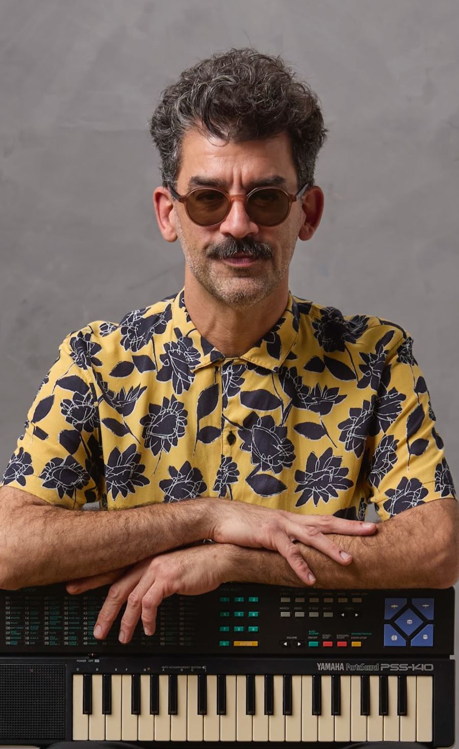 Antonio Boyadjian con anteojos de sol y camisa amarilla, apoyado sobre un teclado Yamaha